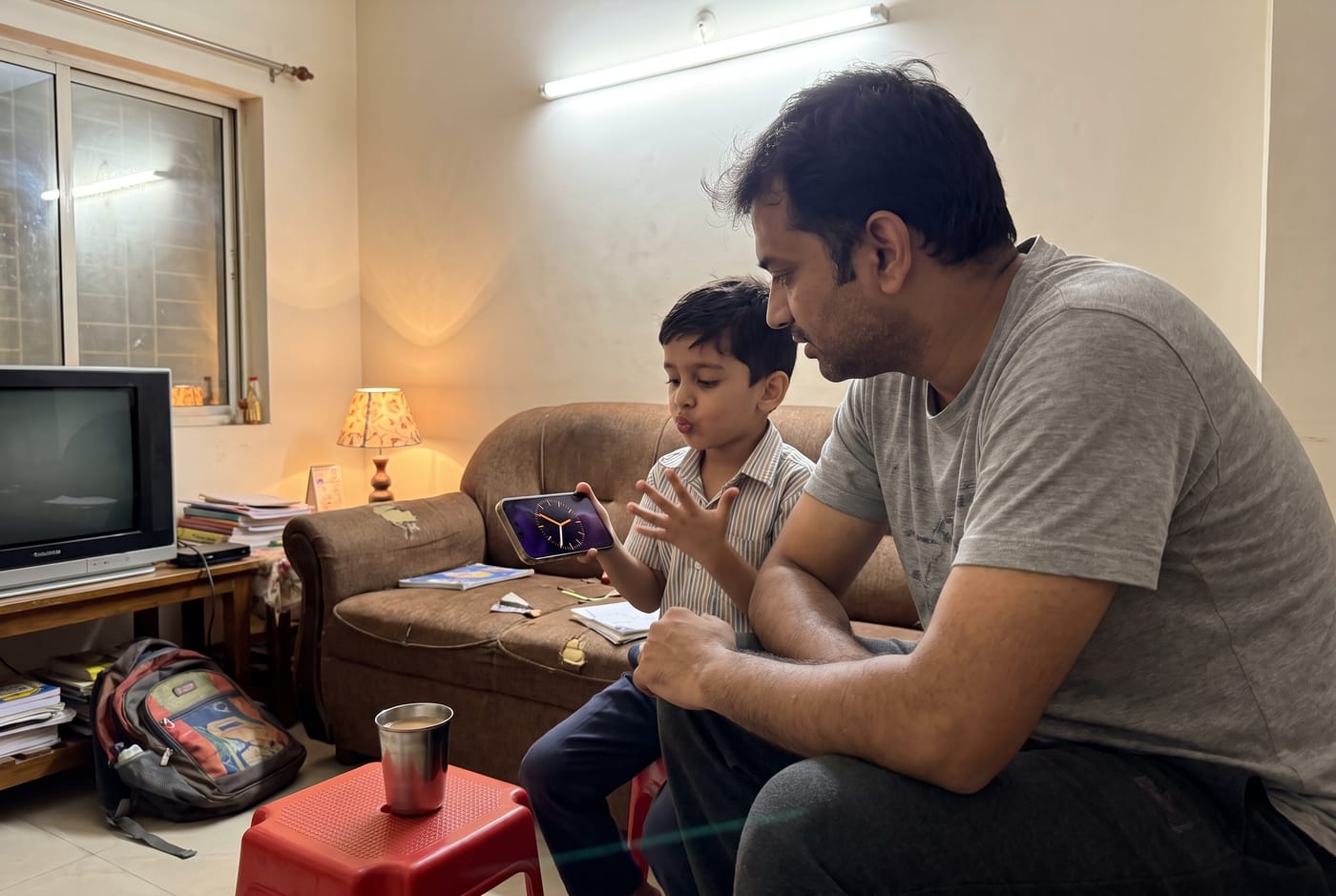 A father and his six-year-old son on a sofa in the evening, the boy counting on his fingers with a phone